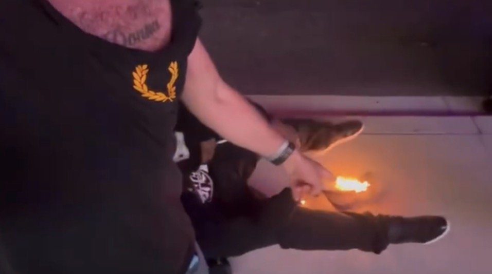A person wearing a black shirt points at a small flame on the ground, demonstrating an unusual and potentially dangerous situation.