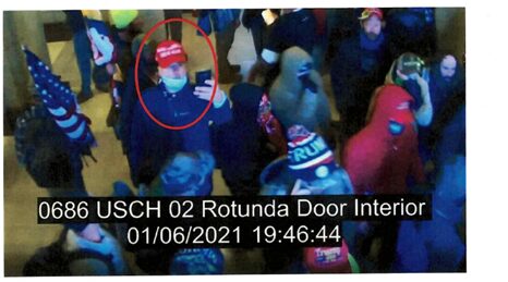 Crowd at the U.S. Capitol Rotunda on January 6, 2021, featuring a person in a red hat and mask using a phone among other attendees.