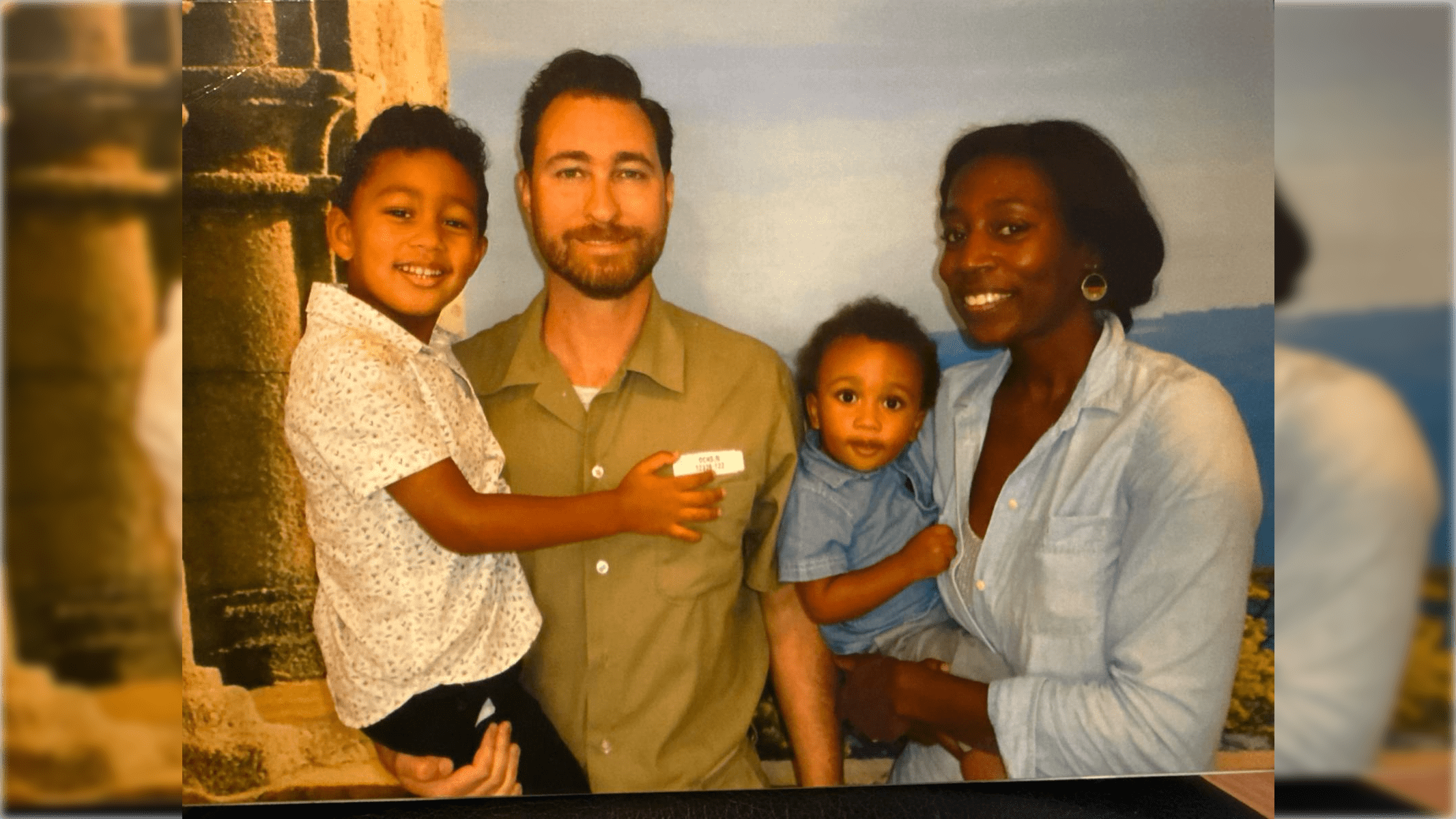 Family portrait featuring a father holding a child, with a mother and another child, set against a scenic background.