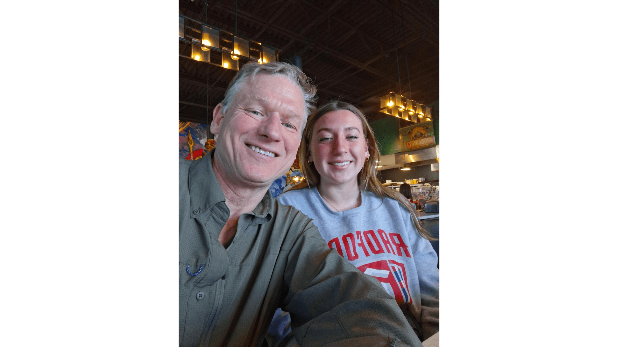 Two smiling individuals take a selfie in a brightly lit café, showcasing a casual atmosphere and colorful artwork in the background.